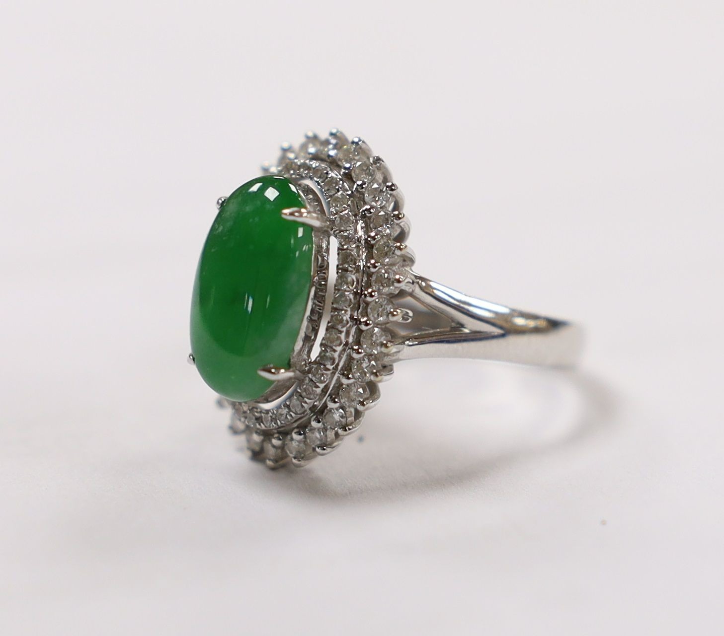 A modern 18k white metal, cabochon jade and two row diamond chip set oval cluster ring size L, gross weight 6.4 grams.